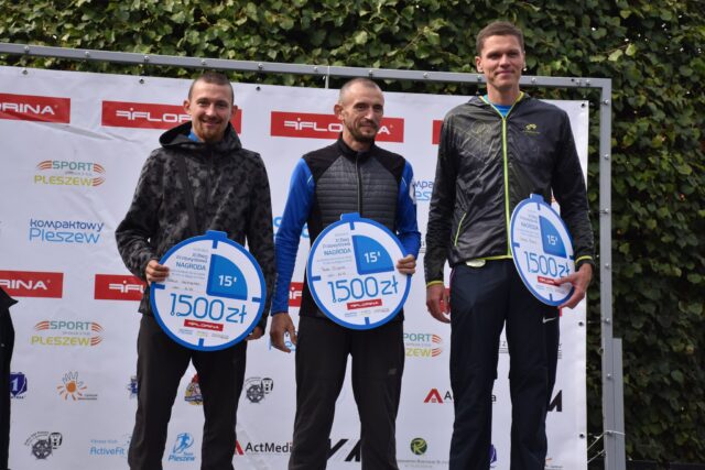 na pierwszym stopniu stoi trójka mężczyzn - zwycięzców Biegu Pzemysława na dystansie 5 km; w ręku trzymają nagrody 