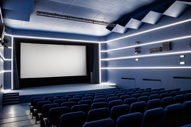 wnętrze kina - widać ekran i kilka pierwszych rzędów krzeseł 