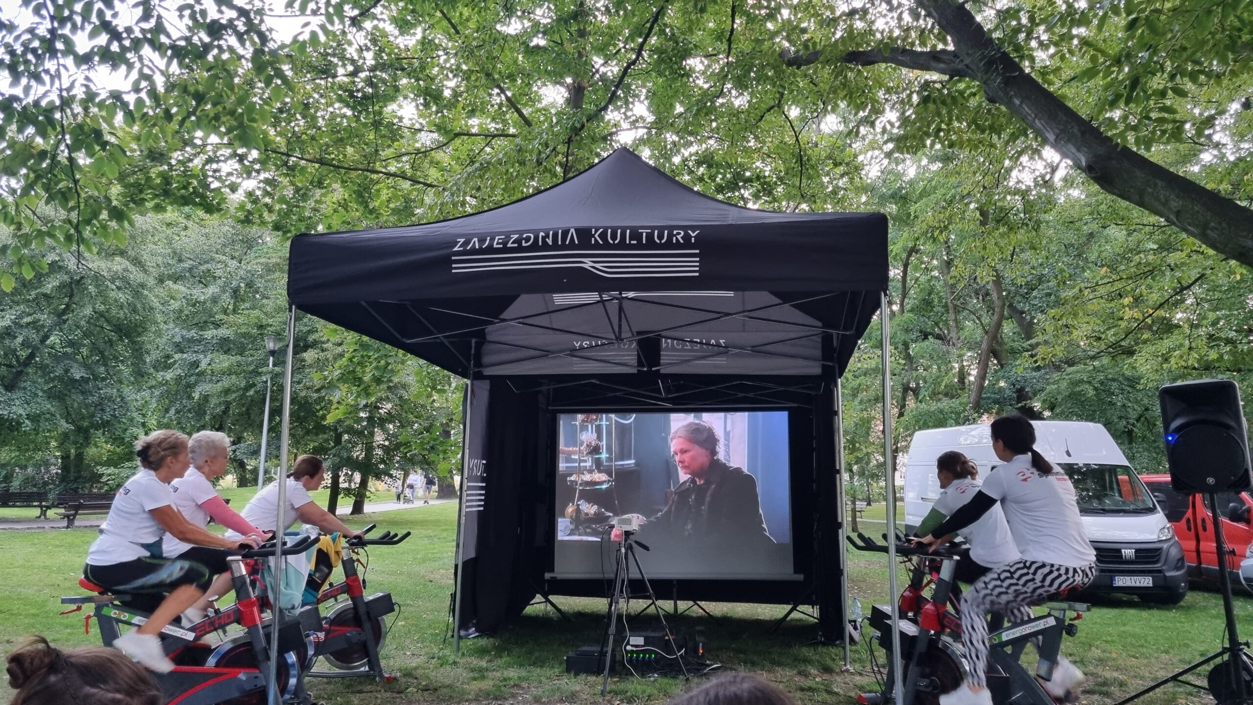 plenerowe kino - w tle ekrankinowy i ludzie jadący na rowerach stacjonarnych napędzających ekran