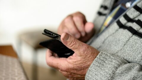zdjęcie przedstawia ręce seniora z telefonem komórkowm