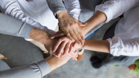 fotografia przedstawia siedem łączących się dłoni symbolizujących wzajemną pomoc