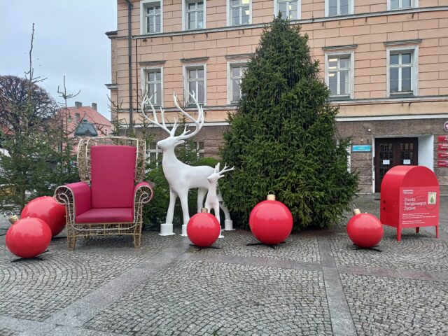 dekoracje świąteczne pleszewskim Rynku w postaci białych reniferów, czerwonego fotela, czerwonych bombek i kilku choinek oraz Poczty Świątecznych Życzeń