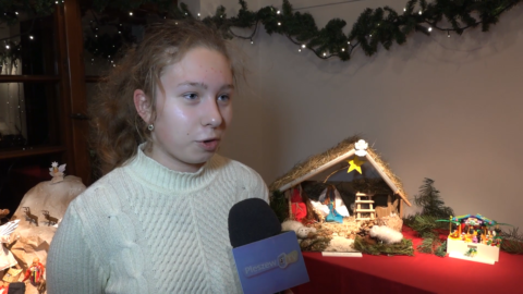 Okładka grudniowego wydania telewizyjnego Flesza PPL przedstawiająca młodą dziewczynę wypowiadającą się do mikrofonu, na tle szopek bożonarodzeniowych
