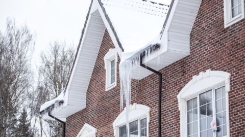 Zdjęcie przedstawia budynek pokryty śnieg oraz zwisające sople lodu z dachu budynku