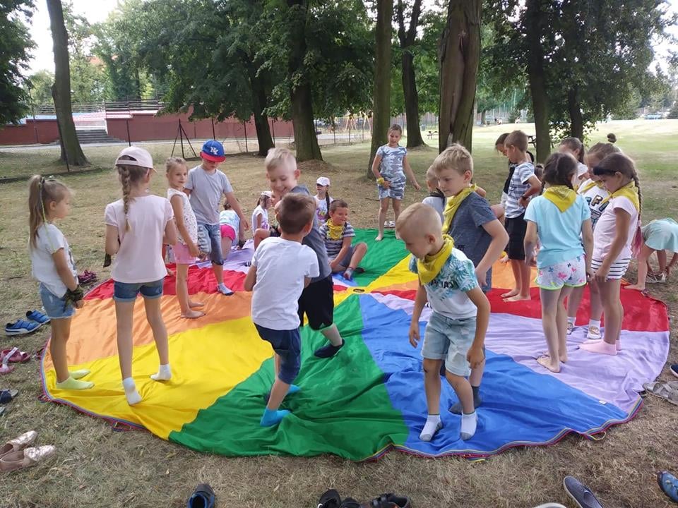 Na zdjęciu znajdują się dzieci podczas animacji z kolorową chustą na terenie amfiteatru przy Stadionie Miejskim w Pleszewie.