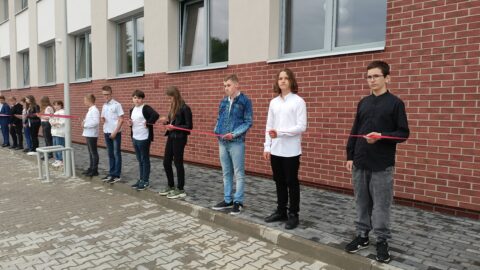 Uczniowie ze wstęgą opasającą całą szkołę w Lenartowicach podczas otwarcia po remoncie.