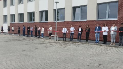 Przecinanie wstęgi opasającej całą szkołę przez uczniów na otwarciu szkoły w Lenartowicach.