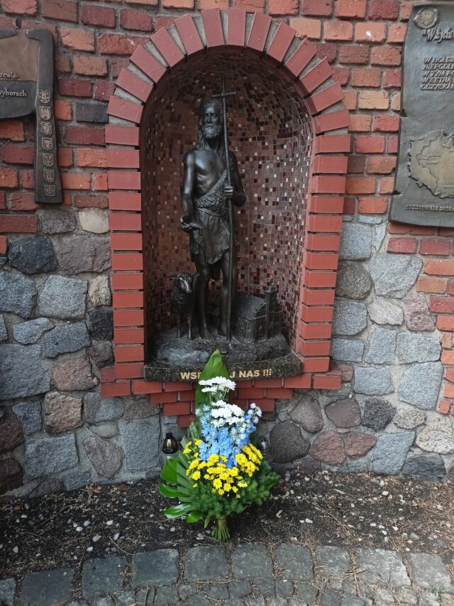 Kwiaty w barwach miasta złożone pod figurą patrona Pleszewa - św. Jana Chrzciciela na Murze Pamięci przy pleszewskiej farze.