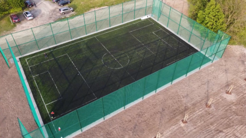 Nowe boisko ze sztuczną nawierzchnią otoczone piłkochwytami w Taczanowie Drugim widziane z lotu ptaka.