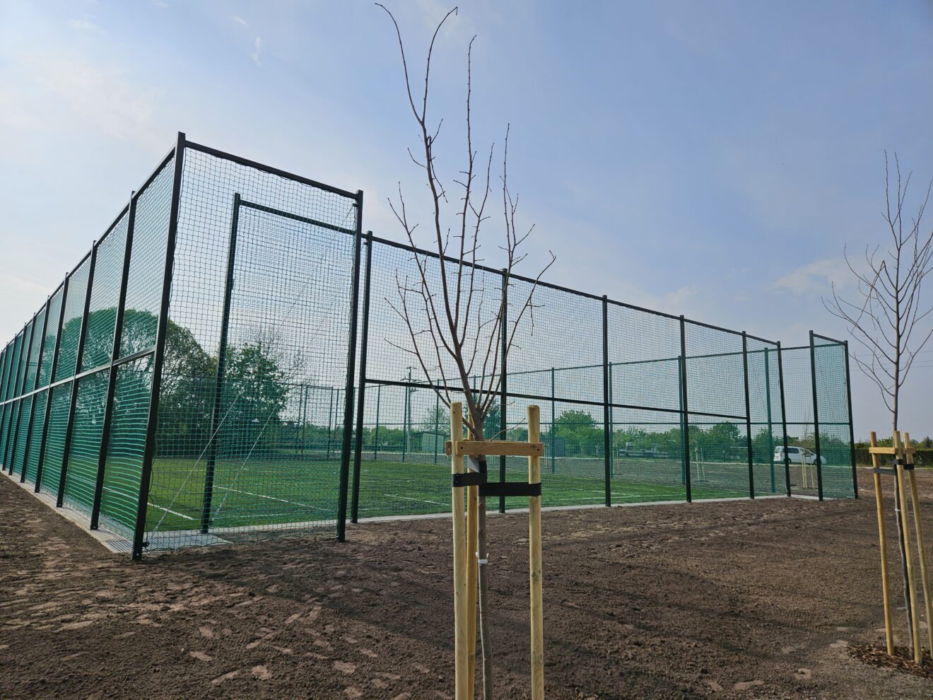 Nowe boisko w Taczanowie Drugim otoczone piłkochwytami oraz drzewa rosnące dookoła.