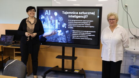 Warsztaty Sztucznej Inteligencji prowadzone przez dwie nauczycielki. w tle ekran z wyświetlaną prezentacją w sali lekcyjnej.
