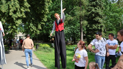 Osoba chodząca na szczudłach i zabawiająca uczestników festynu miejskiego w parku miejskim.
