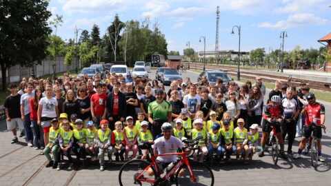 Grupa dzieci i młodzieży z kolarzami na rowerach stojący na parkingu Zajezdni Kultury w Pleszewie.
