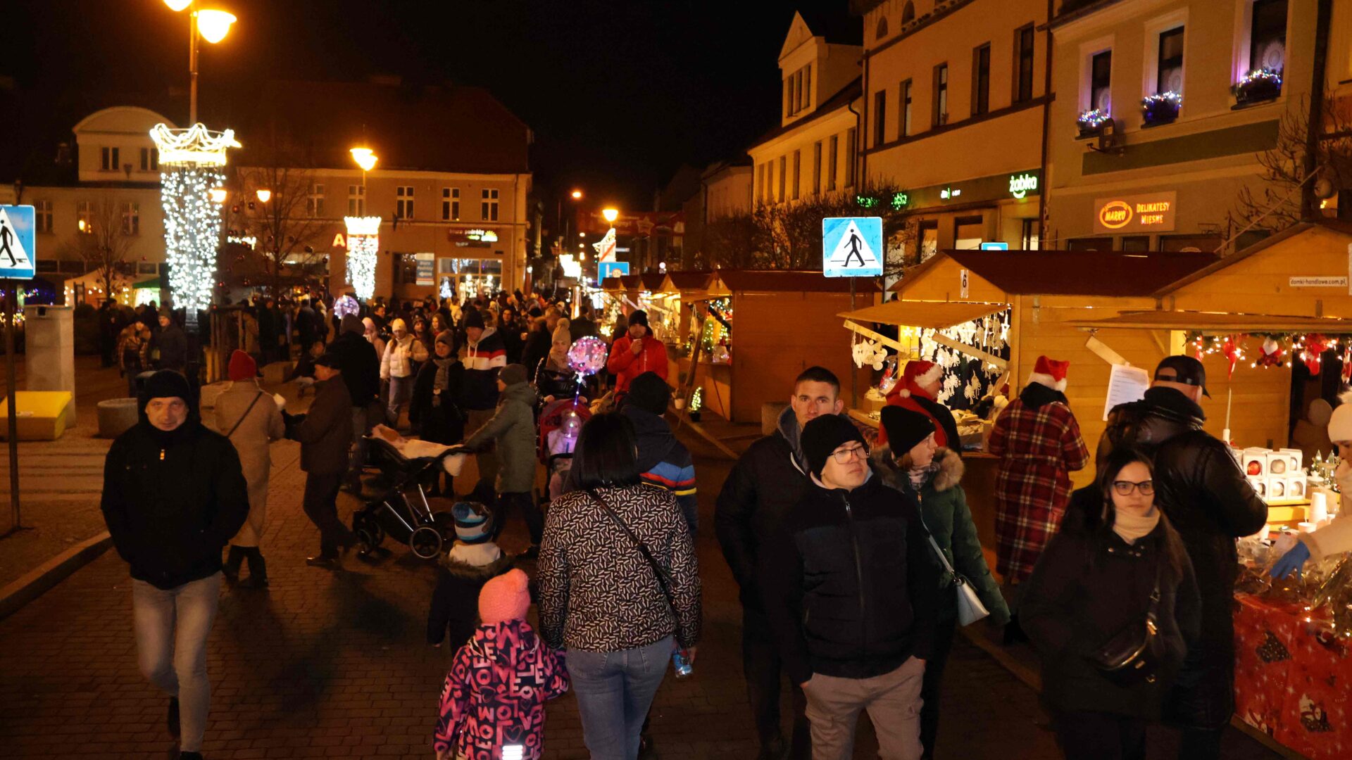 Duża grupa osób odwiedzająca domki handlowe na jarmarku świątecznym w Pleszewie.