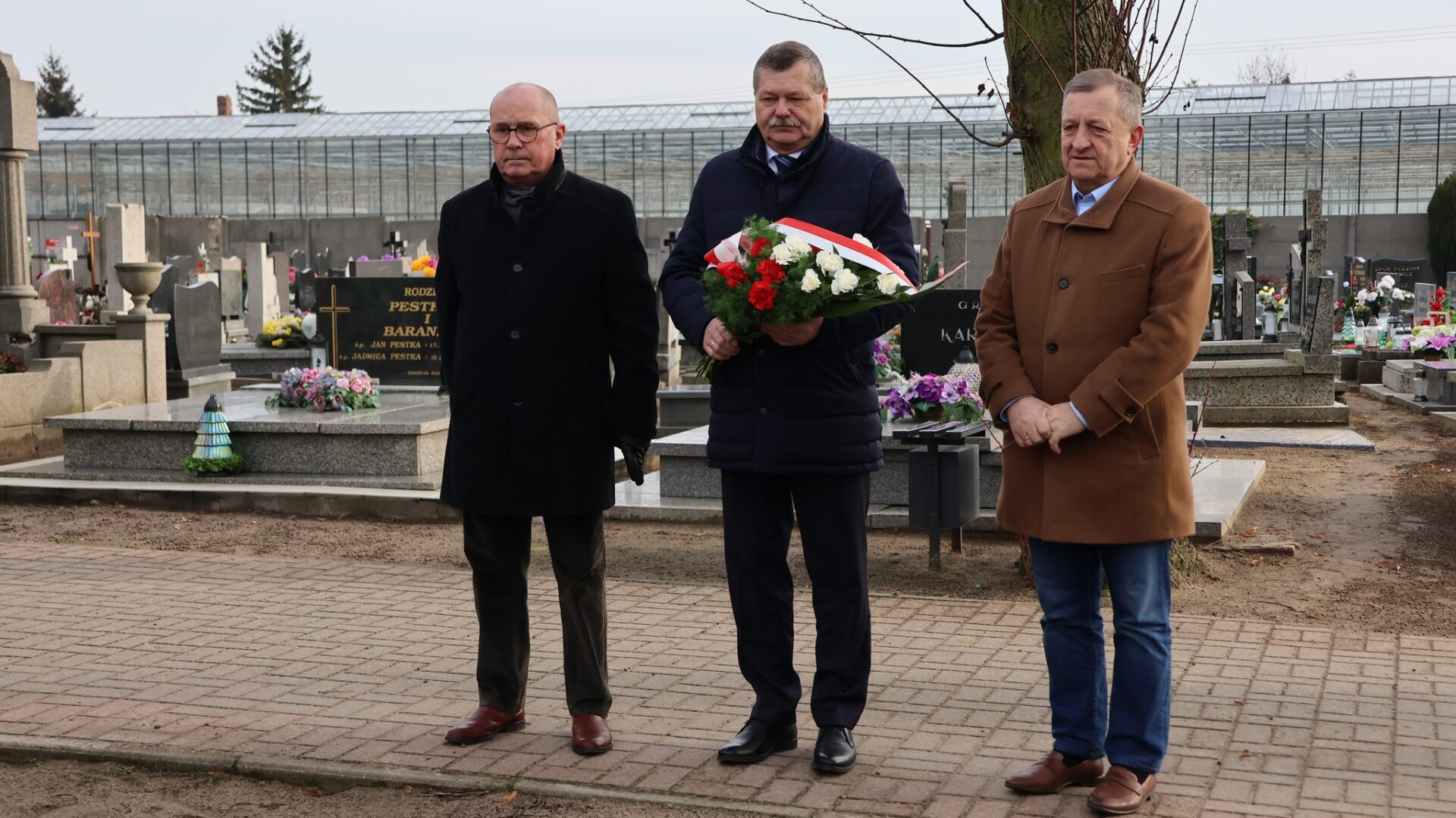 Trzech mężczyzn składających wiązanki kwiatów na grobie.