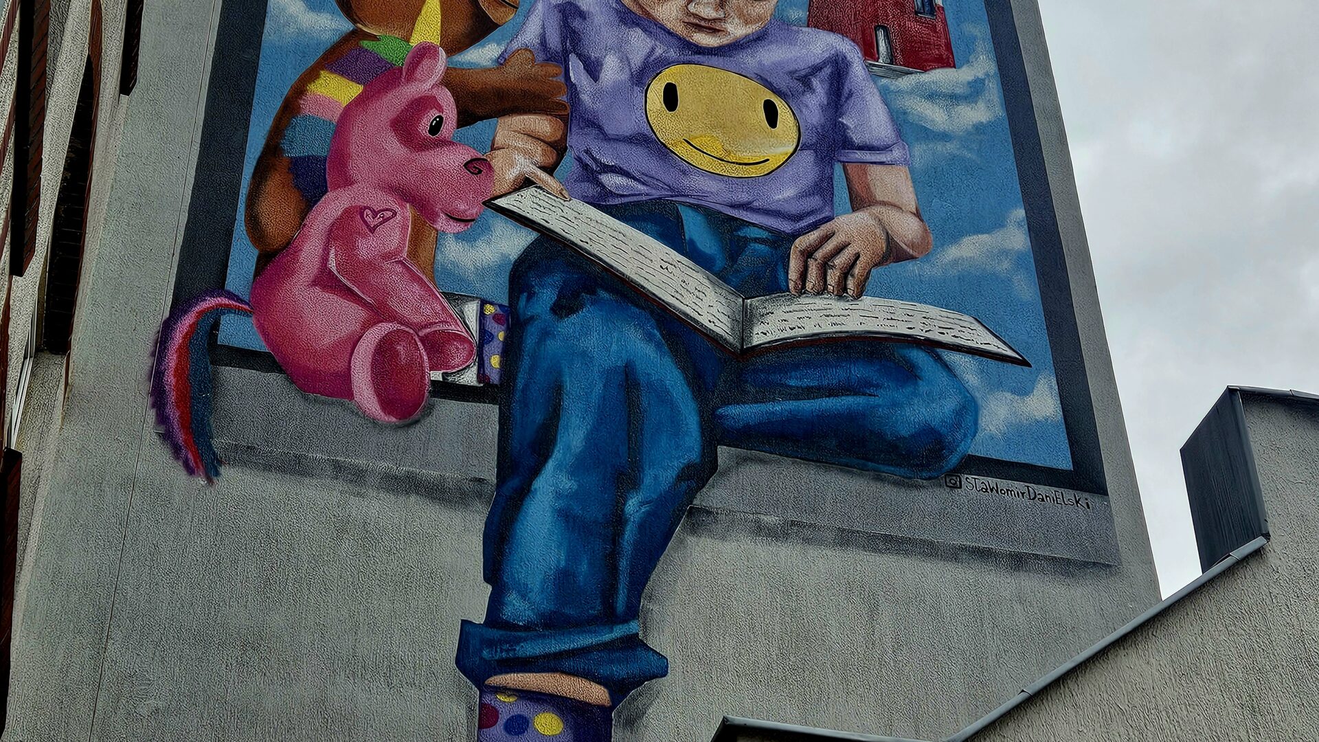 kolorowy wizerunek dziewczynki czytającej książkę na budynku szkoły