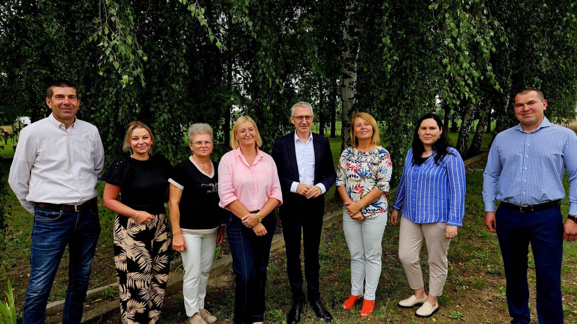 Grupa kobiet i mężczyzn pozujących w plenerze na tle drzew.