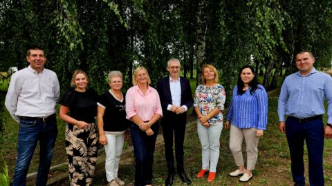 Grupa kobiet i mężczyzn pozujących w plenerze na tle drzew.