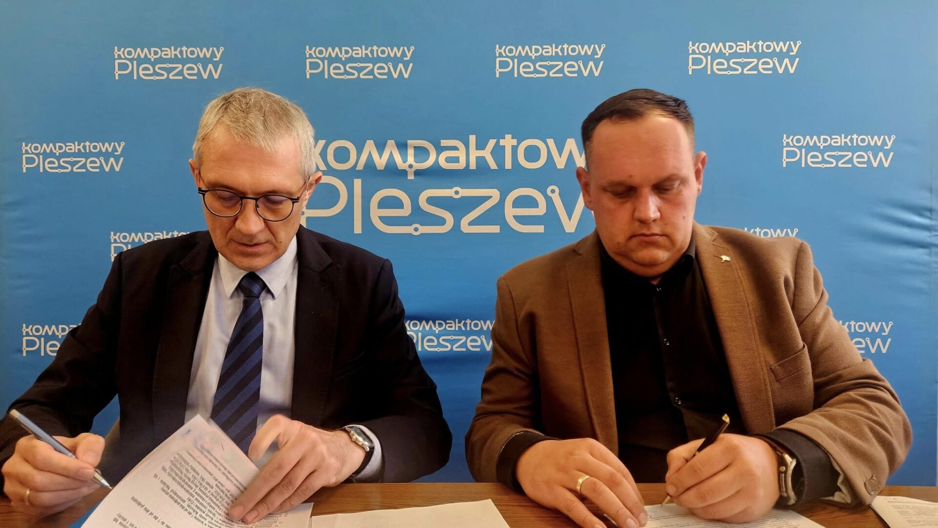 Dwaj mężczyźni podpisujący umowę przy biurku w ratuszu