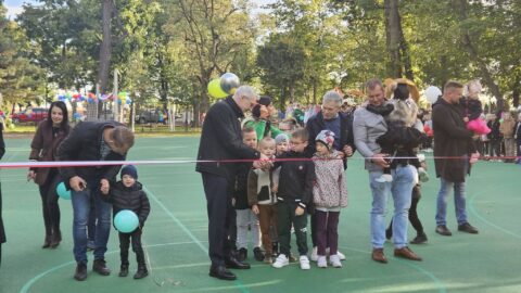 Przecinanie wstęgi przez dorosłe osoby i dzieci na otwarciu wielofunkcyjnego boiska sportowego.