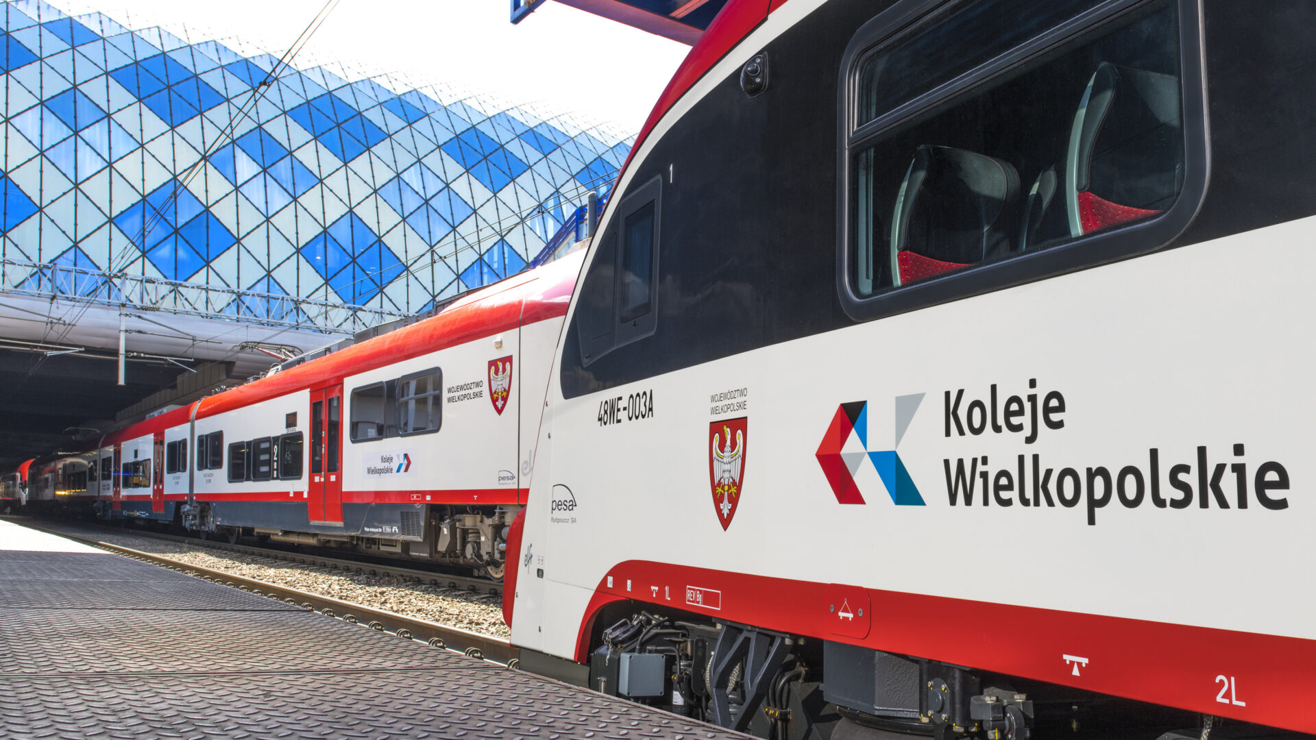 Pociągi Kolei Wielkopolskich stojące na stacji kolejowej.