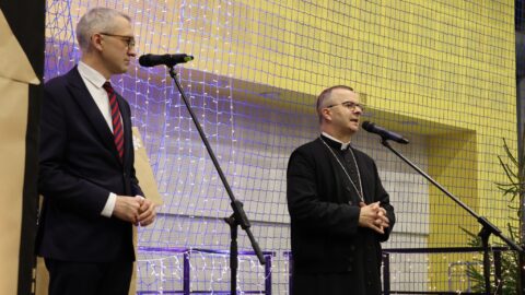 Przemówienie biskupa oraz burmistrza na scenie w hali sportowej podczas Wigilii dla Samotnych w Pleszewie.