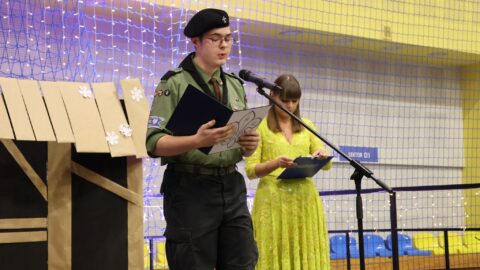 Przemówienie harcerza na scenie w hali sportowej podczas Wigilii dla Samotnych w Pleszewie.
