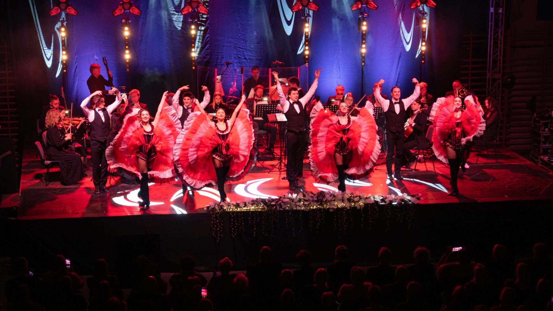 Muzycy i tancerze na scenie hali sportowej podczas koncertu noworocznego.