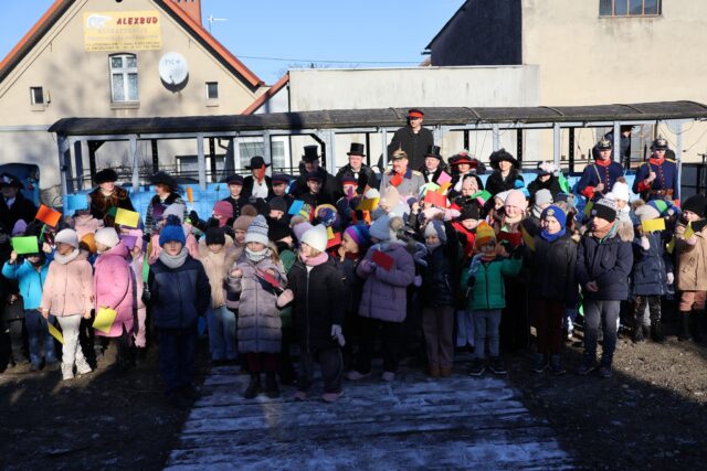 Dzieci ze szkoły witające uczestników historycznego kursu kolejki wąskotorowej na dawnym dworcu przy odkrytych wagonach.