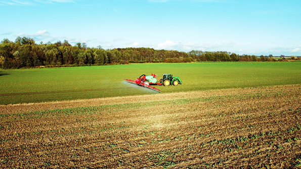 Na zdjęciu znajduje się traktor z opryskiwaczem jeżdżący po polu.