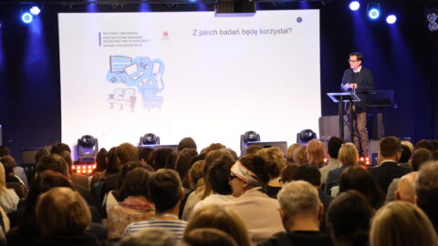 osoba przemawiająca na scenie zajezdni kultury przed liczną widownią