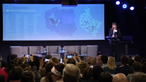 osoba przemawiająca na scenie zajezdni kultury przed liczną widownią