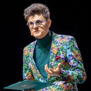 mężczyzna przemawiający na scenie na czarnym tle