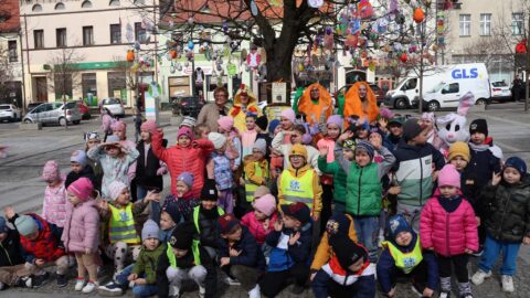Grupa dzieci pozująca po ubraniu drzewek świątecznymi dekoracjami przed budynkiem ratusza.