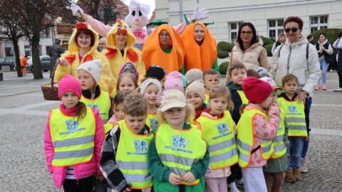 Grupa dzieci pozująca po ubraniu drzewek świątecznymi dekoracjami przed budynkiem ratusza.