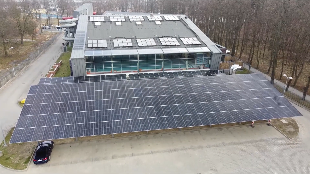 zdjęcie z lotu ptaka przedstawiające parking parku wodnego z zainstalowany panelami fotowoltaicznymi nad miejscami parkingowymi