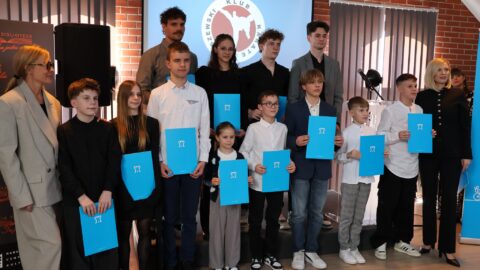 Młodzież stojąca z dyplomami w teczkach podczas wręczania im nagród sportowych.