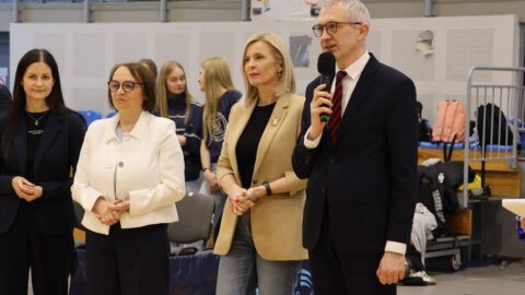 burmistrz przemawiający przed publicznością w hali sportowej podczas zawodów.