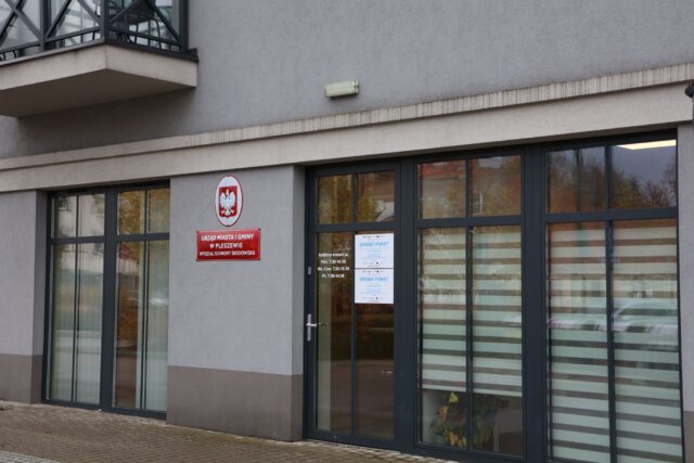 Budynek wielorodzinny z jedną z siedzib Urzędu Miasta i Gminy z przeszklonymi drzwiami i napisami na budynku.