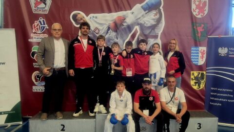 Pleszewska drużyna karate z trenerami na ściance i podium zawodów karate w Tczewie.